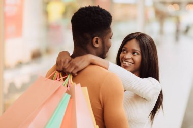 Mutlu siyah çift kucaklaşıyor ve alışveriş torbaları tutuyor.
