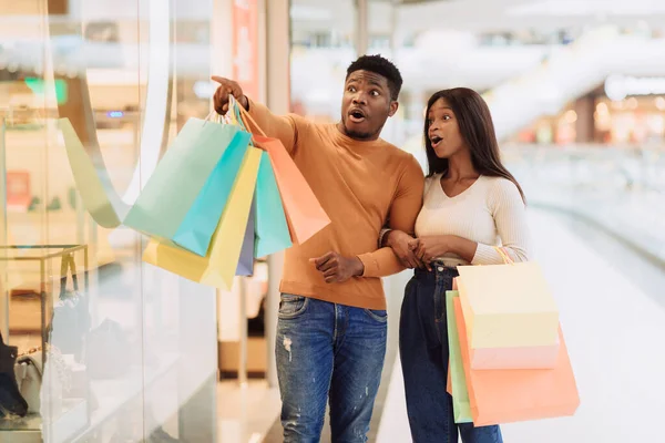 Excited black couple with shopping bags pointing at window — Stock Photo, Image