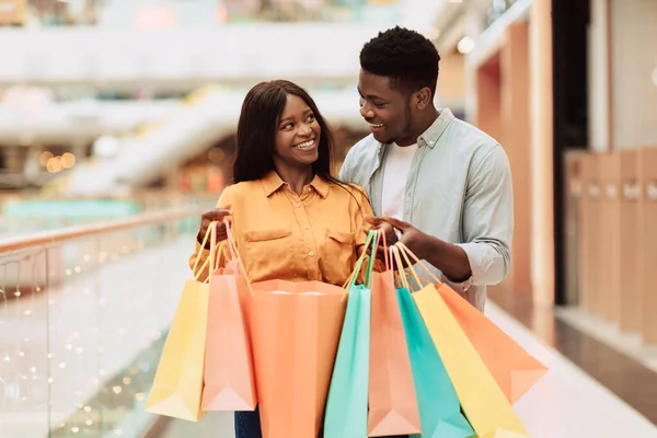 Feliz pareja negra sosteniendo bolsas de compras mirándose —  Fotos de Stock