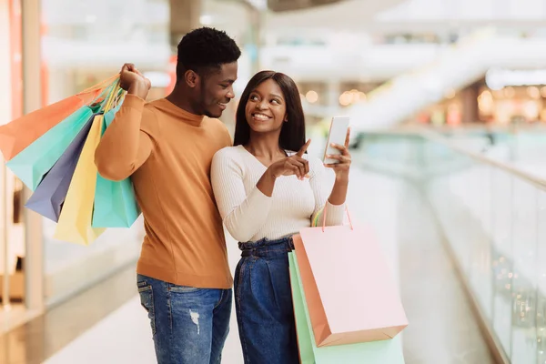 Portrait of happy black couple using phone with shopping bags — Stock Photo, Image