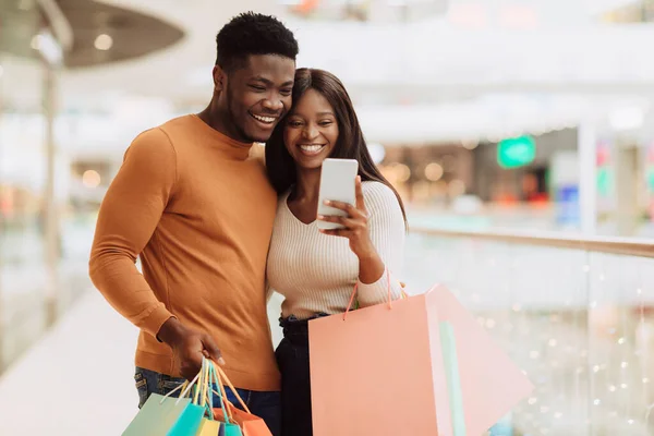 Portret van gelukkig zwart paar met behulp van telefoon met boodschappentassen — Stockfoto