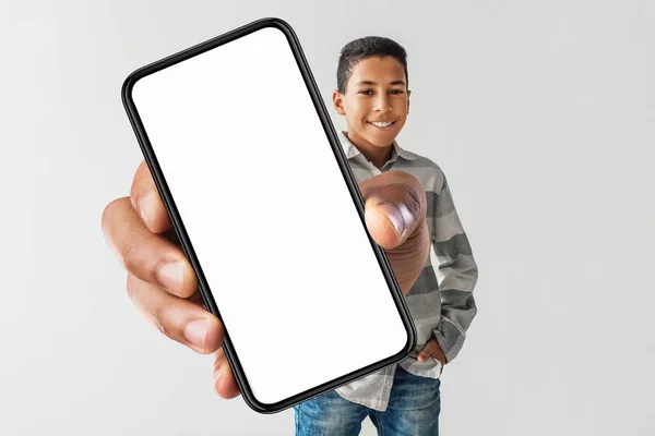 Feliz chico afroamericano sosteniendo enorme Smartphone en fondo gris —  Fotos de Stock