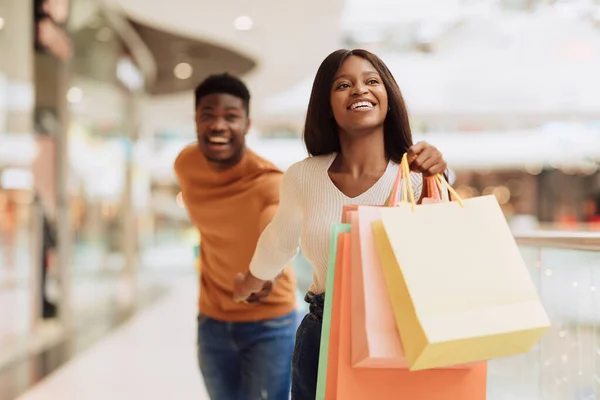 Emocionado negro mujer tirando novio a la tienda de compras —  Fotos de Stock