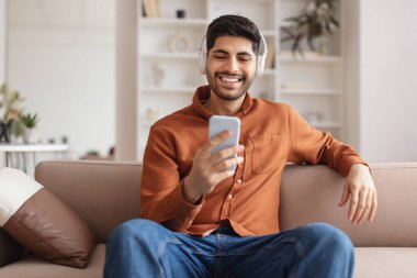 Cep telefonu kullanan, kablosuz kulaklıklı, gülümseyen sakallı adam.