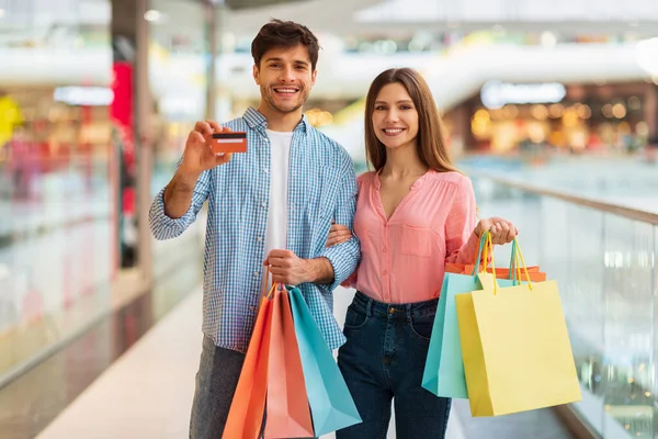 Casal compras mostrando cartão de crédito segurando Shopper sacos no hipermercado — Fotografia de Stock