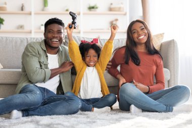 Üç kişilik neşeli Afro-Amerikan ailesi evde video oyunu oynuyorlar.