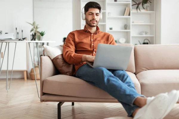 Konzentrierter arabischer Mann mit Kopfhörern benutzt PC zu Hause — Stockfoto