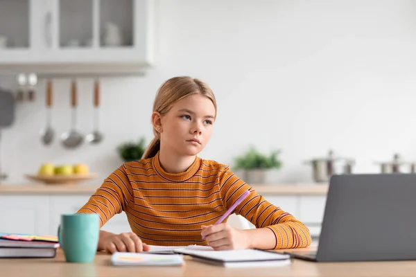 Ciddi beyaz sarışın kız masada oturur, dizüstü bilgisayara bakar, minimalist mutfakta öğrenim görür. — Stok fotoğraf