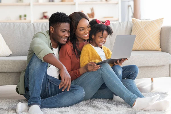 Glad afrikansk amerikansk familj på tre avkopplande med laptop hemma — Stockfoto