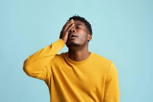 Utmattad svart kille vidrör hans ansikte, blå bakgrund — Stockfoto