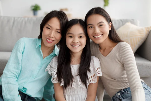 ครอบครัวเอเชียหลายรุ่นที่เป็นบวก โพสและยิ้มที่กล้อง นั่งอยู่บนพื้นในห้องนั่งเล่น — ภาพถ่ายสต็อก