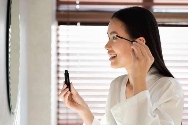 Sidovy över vackra kinesiska damen tillämpa makeup i badrummet — Stockfoto