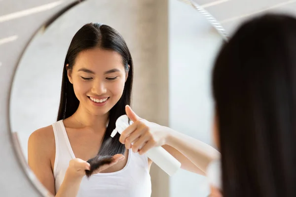 Uzun saçlı mutlu Koreli kadın saç spreyi kullanıyor. — Stok fotoğraf