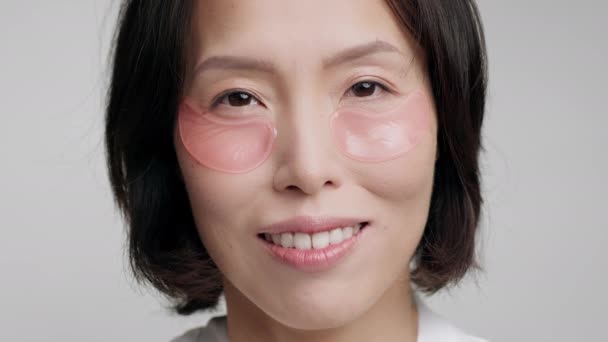 Mujer coreana con parches aplicados bajo los ojos posando en el estudio — Vídeos de Stock