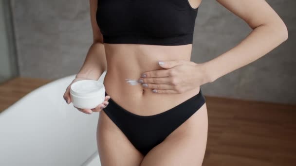Непізнана жінка наносить крем на живіт зволожуючим тілом у ванній — стокове відео