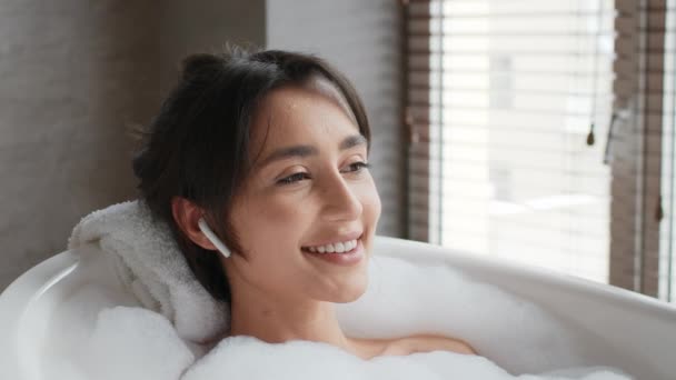 Relaxado feminino tomando banho ouvindo música vestindo fones de ouvido no banheiro — Vídeo de Stock