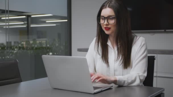 Trabalho de escritório. Jovem gerente em desgaste formal e óculos trabalhando no laptop e sorrindo, tiro de rastreamento, espaço livre — Vídeo de Stock