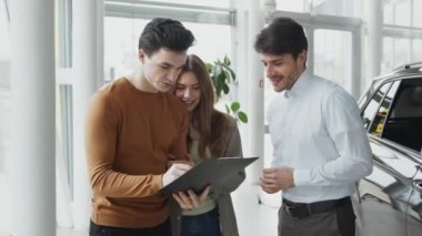 Otomobil galerisinde satış sözleşmesi imzalayan genç adam anlaşmayı kutlamak için satış temsilcisiyle el sıkışıyor, yakınlaştırıyor.