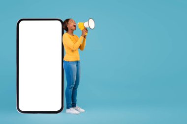Heyecanlı siyah kadın büyük boş akıllı telefonun yanında dururken megafona bağırıyor.