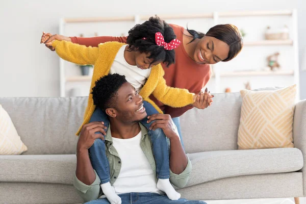 Atividades familiares. Pais negros felizes se divertindo com a pequena filha em casa — Fotografia de Stock