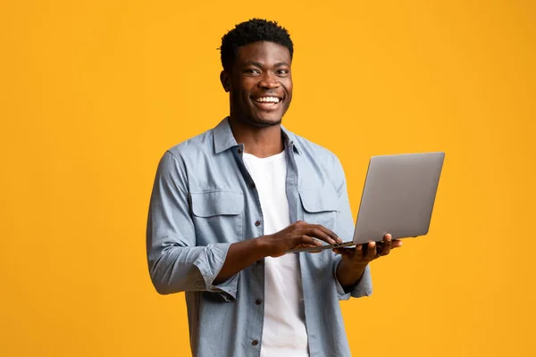 Przystojny czarny człowiek za pomocą nowoczesnego laptopa na żółty — Zdjęcie stockowe