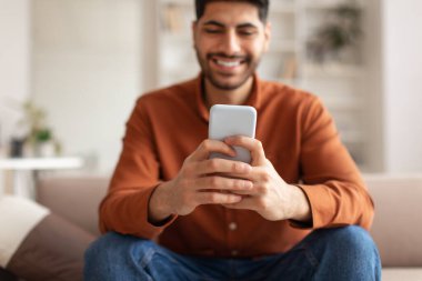 Evde akıllı telefon kullanan gülümseyen bir Arap.