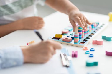 Küçük çocukların elleri mantıksal ahşap oyunlarla oynarken profesyonel kadın terapist not alıyor.