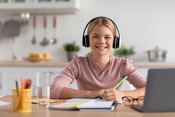 Gai européen adolescent fille blonde dans casque étude à la maison à la table avec ordinateur portable dans cuisine intérieur — Photo