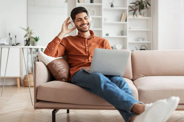 Usmívající se Arab muž používá PC doma, poslouchá hudbu — Stock fotografie