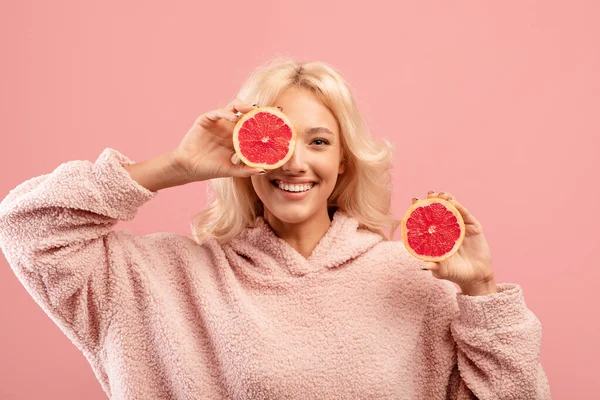 Vitaminas para beleza e cuidados com a pele. Senhora caucasiana feliz posando com metades de toranja no fundo do estúdio rosa — Fotografia de Stock