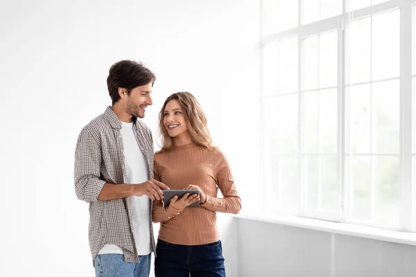 Joven europeo alegre y señora en habitación vacía con ventana panorámica, tableta de retención y diseño de planificación —  Fotos de Stock