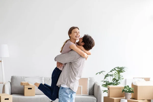 Satisfecho europeo joven marido levanta y abraza a su esposa en el interior de la habitación divertirse juntos —  Fotos de Stock