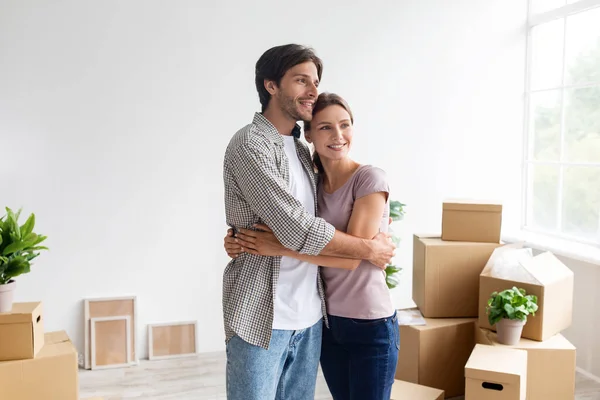 Feliz casal milenar europeu em abraços casuais e descansar no quarto com caixas de papelão, desfrutar da compra de novo apartamento — Fotografia de Stock