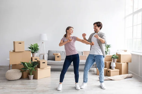 Glad happy european millennial guy and female have fun dancing together in room interior among boxes