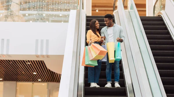 Feliz pareja negra sosteniendo bolsas de compras va en escaleras mecánicas —  Fotos de Stock
