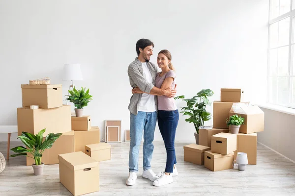 Blij Europese duizendjarige vrouw en echtgenoot in casual knuffelen in kamer met kartonnen dozen, genieten van het kopen van nieuw appartement — Stockfoto