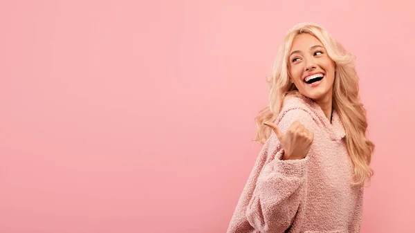 Check this. Excited blonde lady looking and pointing back at free space for advertisement, pink background, panorama — Stock Photo, Image