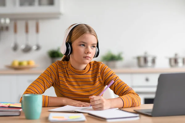 Concentré européen adolescent blonde fille dans les écouteurs assis à la table regarder la leçon vidéo sur ordinateur portable — Photo