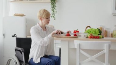 Günlük rutin ve maluliyet. Orta yaşlı kadın tekerlekli sandalye kullanıcısı sağlıklı yemek pişiriyor, mutfakta sebze kesiyor.