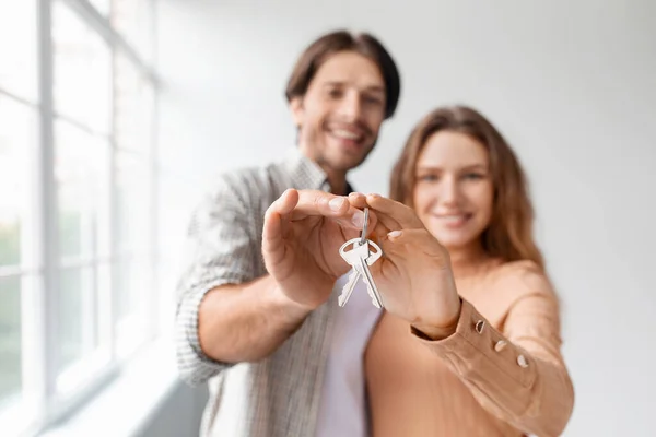 Glad happy caucasian young male and female in empty room with panoramic window, show keys — Stock Photo, Image