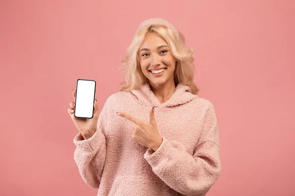 Gran aplicación móvil o sitio web. Mujer joven feliz sosteniendo un teléfono inteligente moderno y apuntando a la pantalla vacía blanca — Foto de Stock