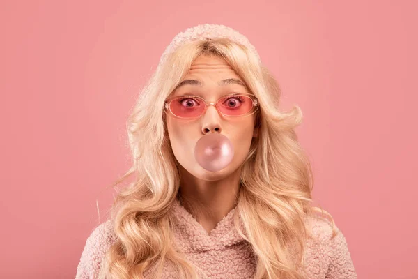 Glada blond dam tuggummi och blåsa bubbla, tittar på kameran på rosa studio bakgrund — Stockfoto