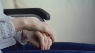 Engelli bir kadın ellerini ovuşturuyor, acıdan acı çekiyor ve donmuş hissediyor, tekerlekli sandalyede oturuyor.