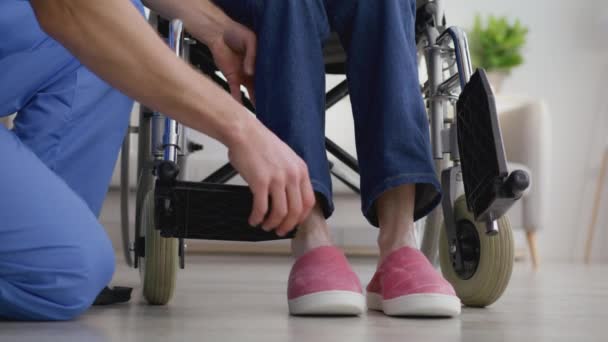 Заботиться о людях с ограниченными возможностями. Закрытие профессиональной коляски, помогающей инвалиду-колясочнику поставить ноги на подножки — стоковое видео