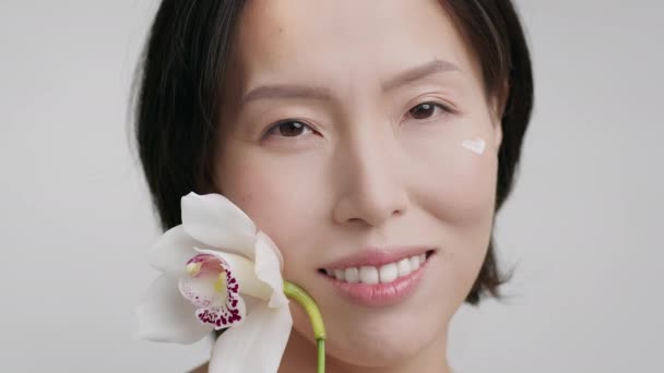 Asiatique moyen âge dame avec visage crème tenant orchidée, studio — Video