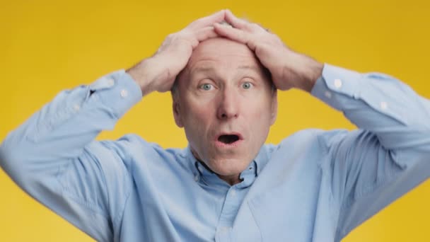Notícias chocantes. Homem sênior incrível agarrando sua cabeça de cabelos grisalhos, sentindo-se surpreso e afetado, fundo amarelo — Vídeo de Stock