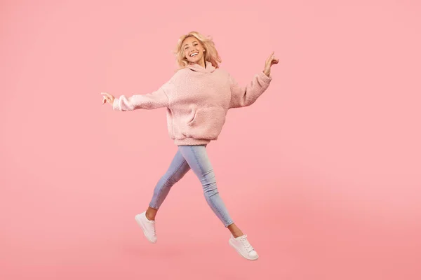 Радостная стильная женщина бегает и прыгает, позирует в воздухе на фоне розовой студии, копирует пространство — стоковое фото