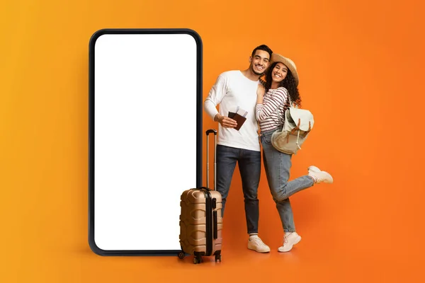 Amar pareja joven posando cerca de enorme teléfono inteligente con pantalla blanca vacía, ofreciendo publicidad agencia de viajes, maqueta — Foto de Stock
