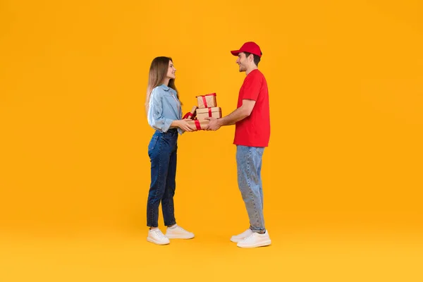 Courier dando caixas de presente para a mulher do cliente sobre fundo amarelo — Fotografia de Stock