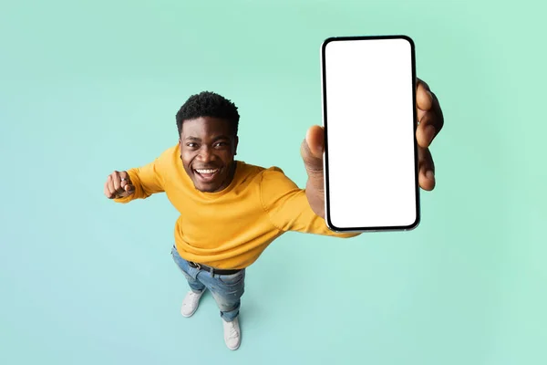 Pria kulit hitam yang bersemangat mendemonstrasikan smartphone dengan layar putih kosong, menampilkan ruang kopi gratis untuk iklan Anda, mockup — Stok Foto
